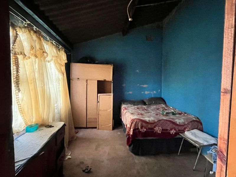 A bedroom featuring exposed roof rafters and corrugated sheeting, requiring significant cosmetic updates and wall repairs to improve the overall condition.
