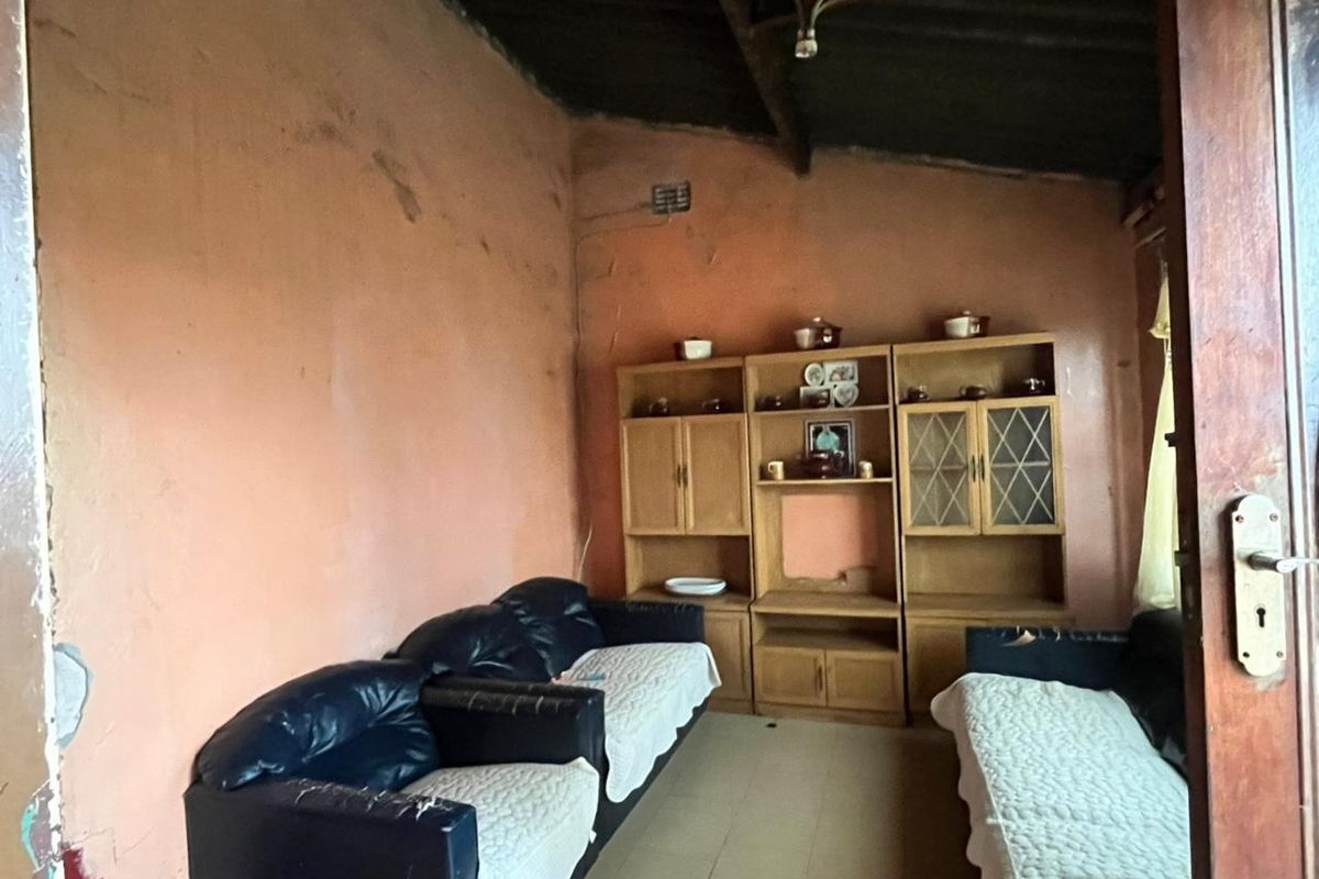 A living room space featuring exposed rafters and tiled flooring, currently requiring significant cosmetic updates and wall repairs to improve its overall condition.