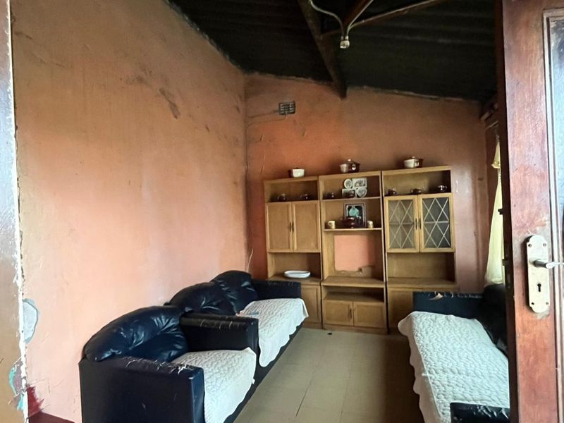 A living room space featuring exposed rafters and tiled flooring, currently requiring significant cosmetic updates and wall repairs to improve its overall condition.