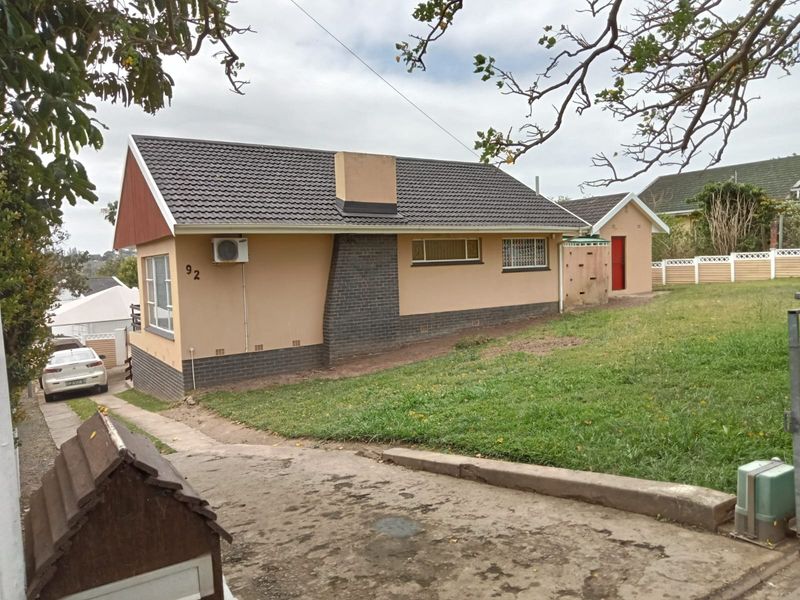 Front exterior view of a single-story house featuring a tiled roof, brick chimney, and concrete driveway with surrounding lawn area.