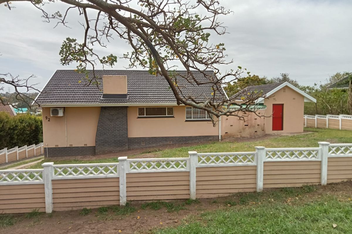 Rear view of the property featuring a tiled roof, brick chimney, and a detached outbuilding, enclosed by a precast concrete boundary wall.