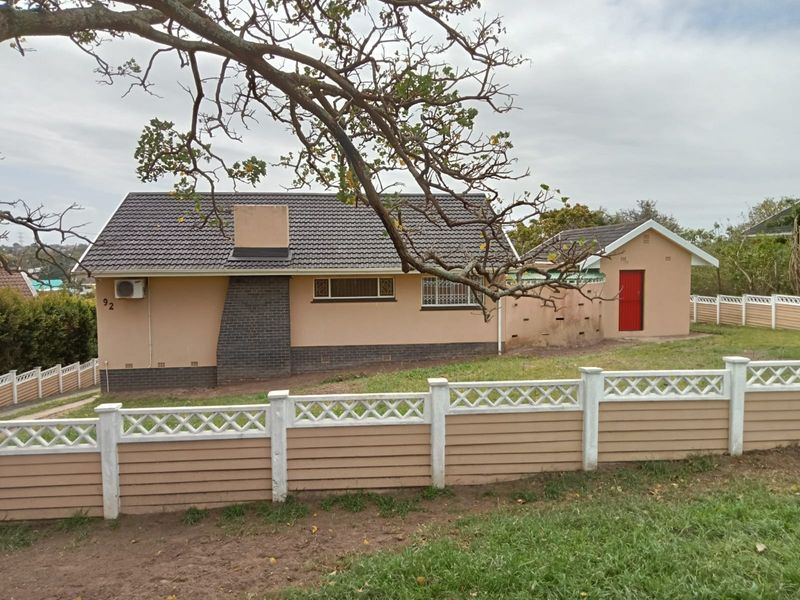 Rear view of the property featuring a tiled roof, brick chimney, and a detached outbuilding, enclosed by a precast concrete boundary wall.