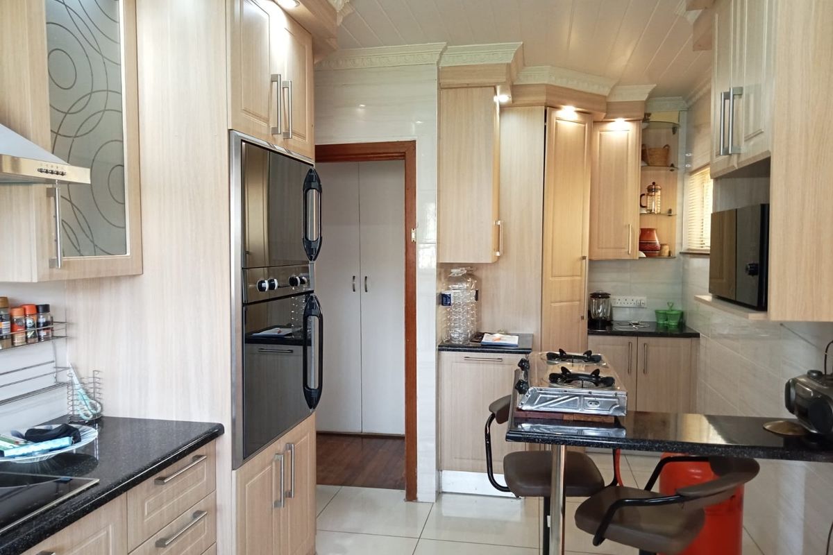 A well-maintained kitchen featuring light wood cabinetry, granite countertops, built-in oven, and an extractor fan, with tiled flooring and coved ceiling details.