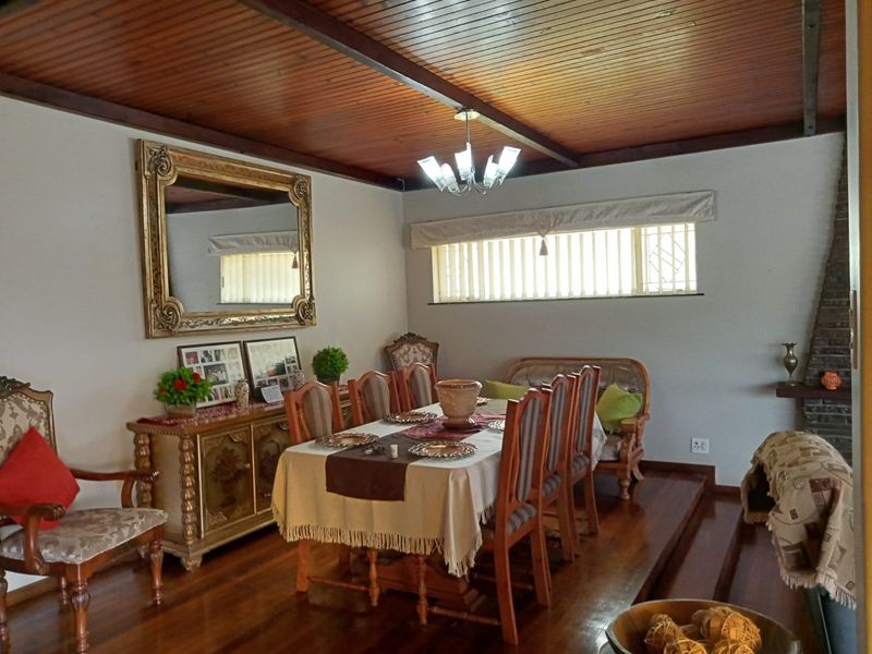 Dining room featuring a timber ceiling, hardwood flooring, a raised floor platform, and a brick fireplace, offering a traditional and warm atmosphere.