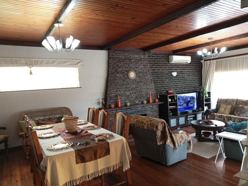 Spacious open-plan living and dining area featuring a striking stone fireplace, timber-clad vaulted ceilings with exposed beams, and polished hardwood flooring.