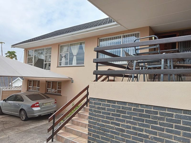 Front exterior view of the property featuring a tiled roof, brick facade, staircase with railings, and a covered carport area.