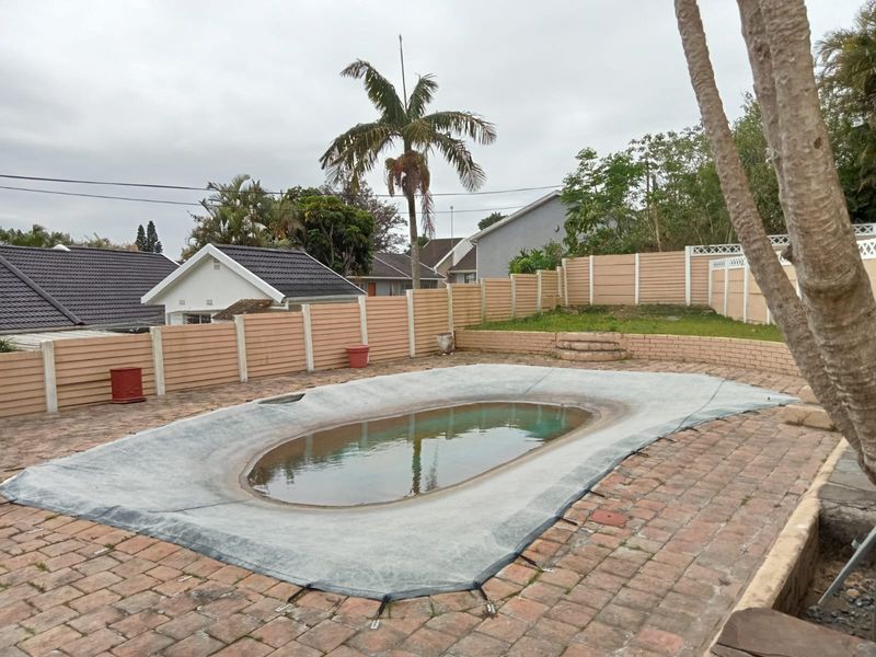 Outdoor pool area featuring a paved surround, retaining wall, and precast boundary fencing, currently covered and requiring maintenance.