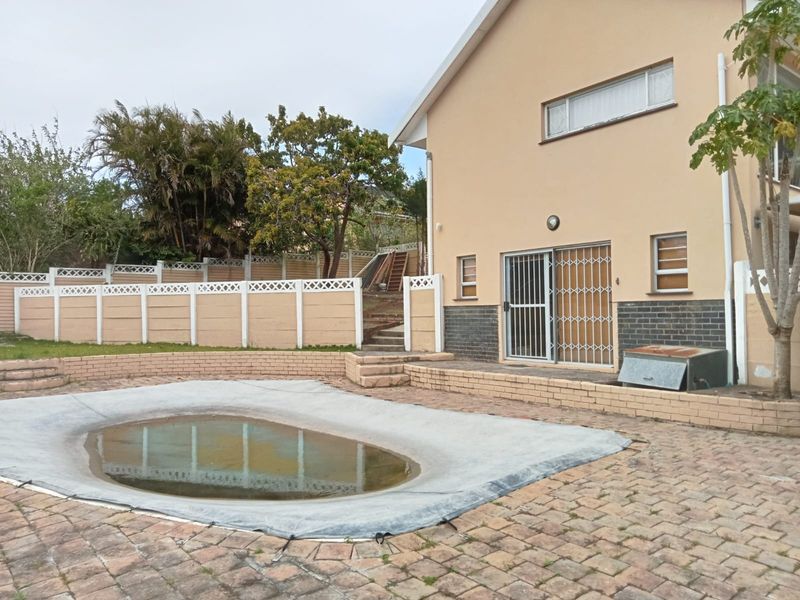 Rear exterior view featuring a swimming pool with a cover, brick paved patio area, and a secure boundary wall.
