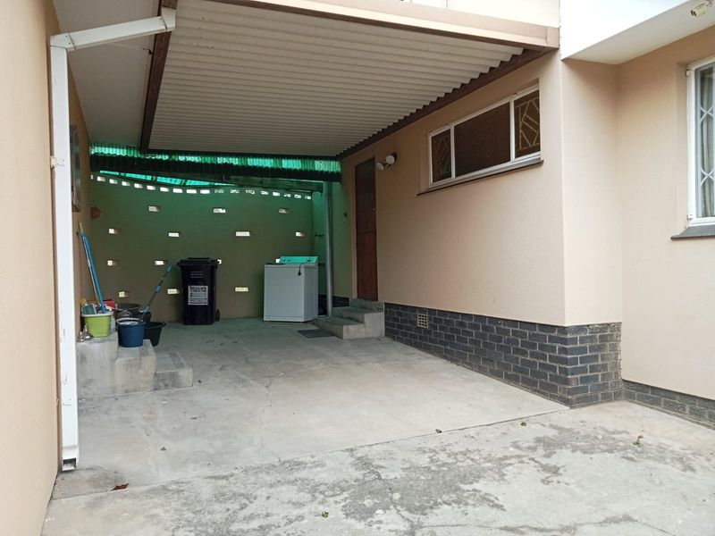 A covered outdoor patio area featuring concrete flooring and a corrugated roof, providing a functional space for utility or outdoor storage.