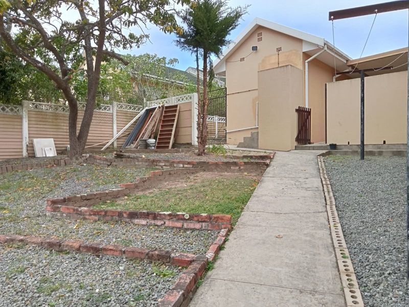 Rear exterior view of the property featuring a concrete walkway, gravel landscaping, and tiered brick retaining walls with visible exterior wall staining.