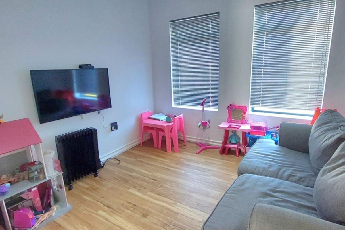 A living room featuring hardwood flooring and dual windows with fitted venetian blinds, providing a functional space for relaxation.