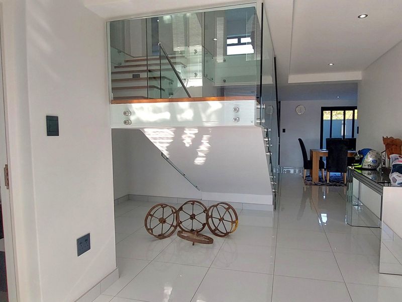 Modern entrance hall featuring a striking timber staircase with glass balustrade, polished porcelain flooring, and an adjacent guest bathroom with a floating vanity.