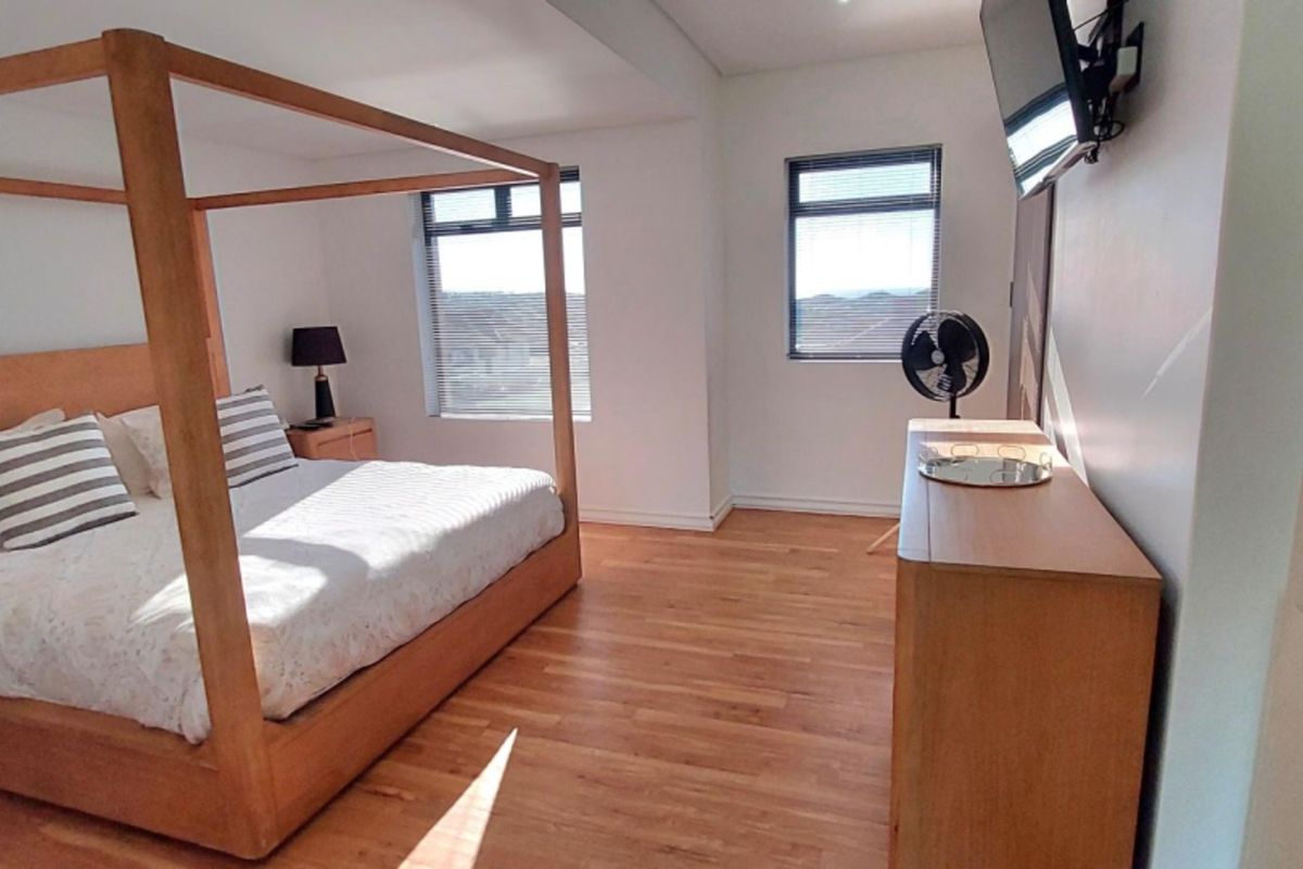 A spacious bedroom featuring hardwood flooring, built-in shelving, and large windows that provide ample natural light.