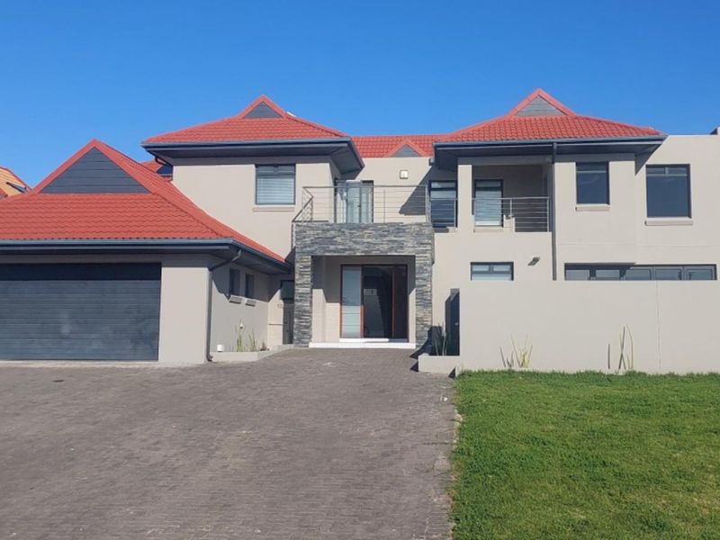 A modern double-story house featuring a tiled roof, stone-clad entrance, balcony, and a paved driveway leading to a double garage.