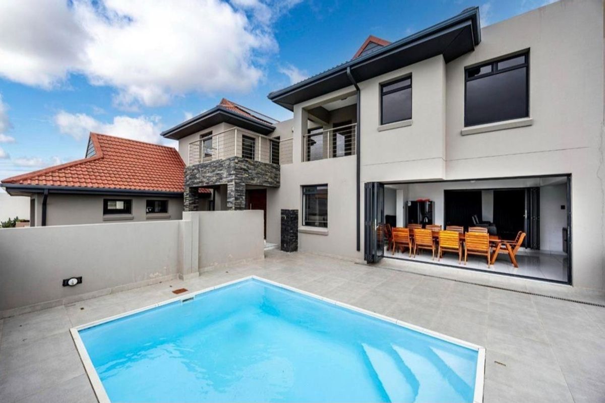 Modern double-story residence featuring a swimming pool, tiled patio area, and large bi-fold doors connecting the indoor and outdoor living spaces.