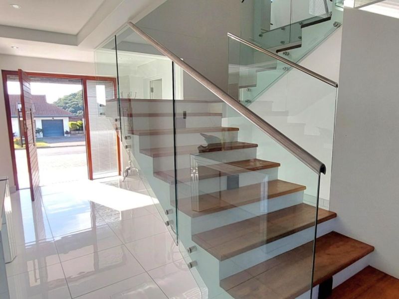 Modern entrance hall featuring a timber staircase with a contemporary glass balustrade and polished tiled flooring.