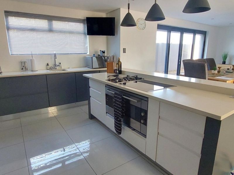 Modern open-plan kitchen featuring a central island with built-in oven and gas hob, sleek cabinetry, stone countertops, and seamless flow to the dining area.