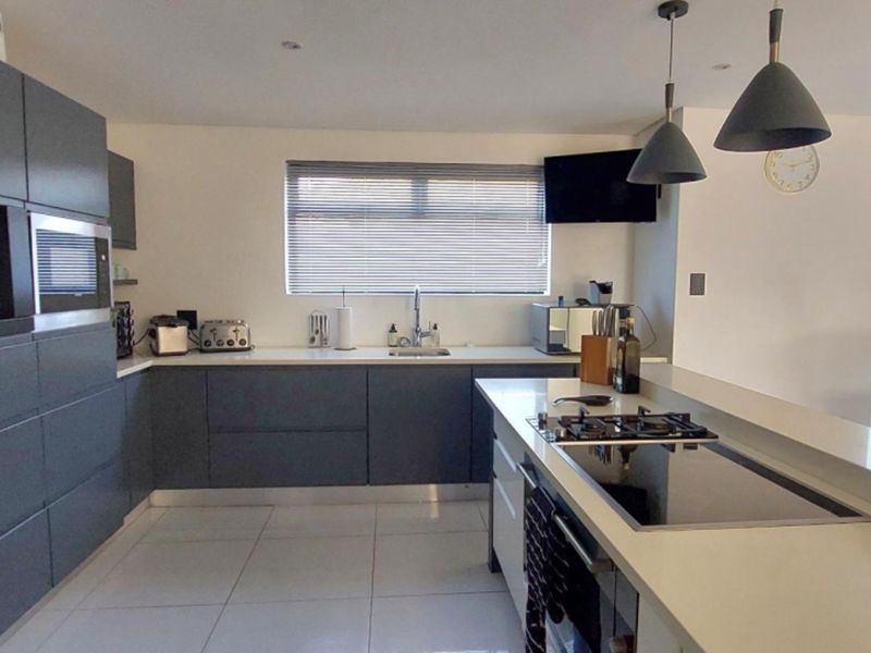 Modern kitchen featuring dark grey cabinetry, stone countertops, integrated appliances, gas cooktop, and tiled flooring with direct access to the outdoor area.