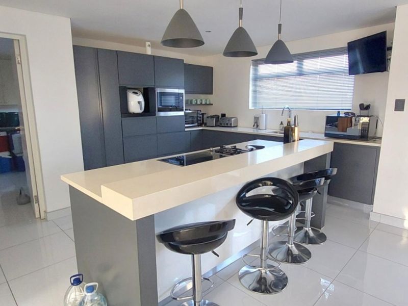 Modern kitchen featuring a central island with a built-in hob, stone countertops, sleek dark cabinetry, and contemporary pendant lighting.