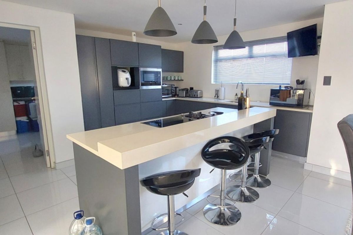 Modern kitchen featuring a central island with a built-in hob, stone countertops, sleek dark cabinetry, and contemporary pendant lighting.