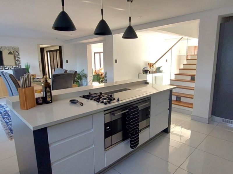Modern open-plan living area featuring a sleek kitchen island with integrated appliances, tiled flooring, and a contemporary staircase with timber treads and glass balustrade.