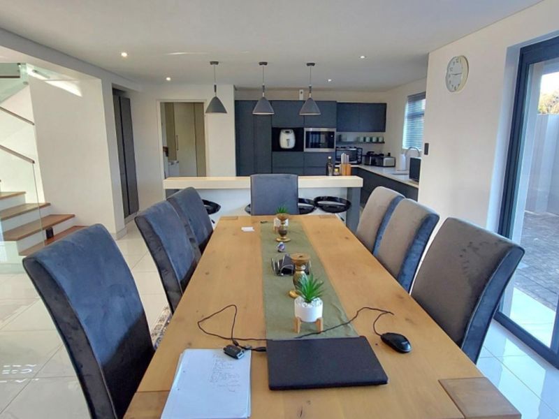 Modern open-plan living and dining area featuring a sleek kitchen with built-in appliances, tiled floors, and a staircase with a glass balustrade.