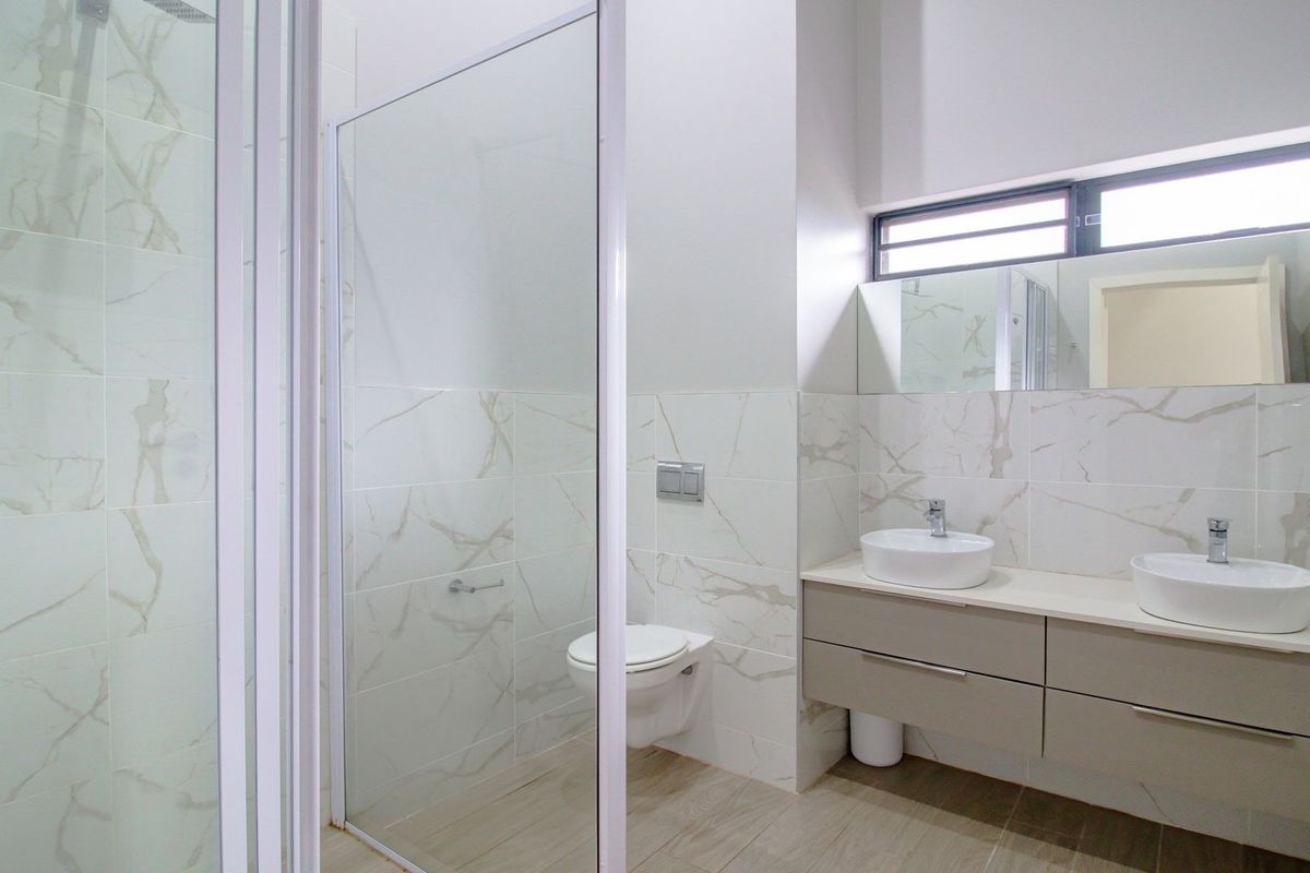 Modern bathroom featuring a double vanity with countertop basins, a wall-mounted toilet, and a spacious glass-enclosed shower with marble-look wall tiling.