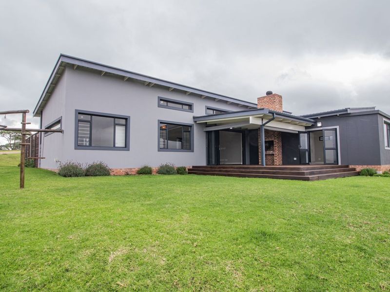 Rear view of a modern house featuring a covered patio with timber decking, a built-in braai, and a spacious lawn area.