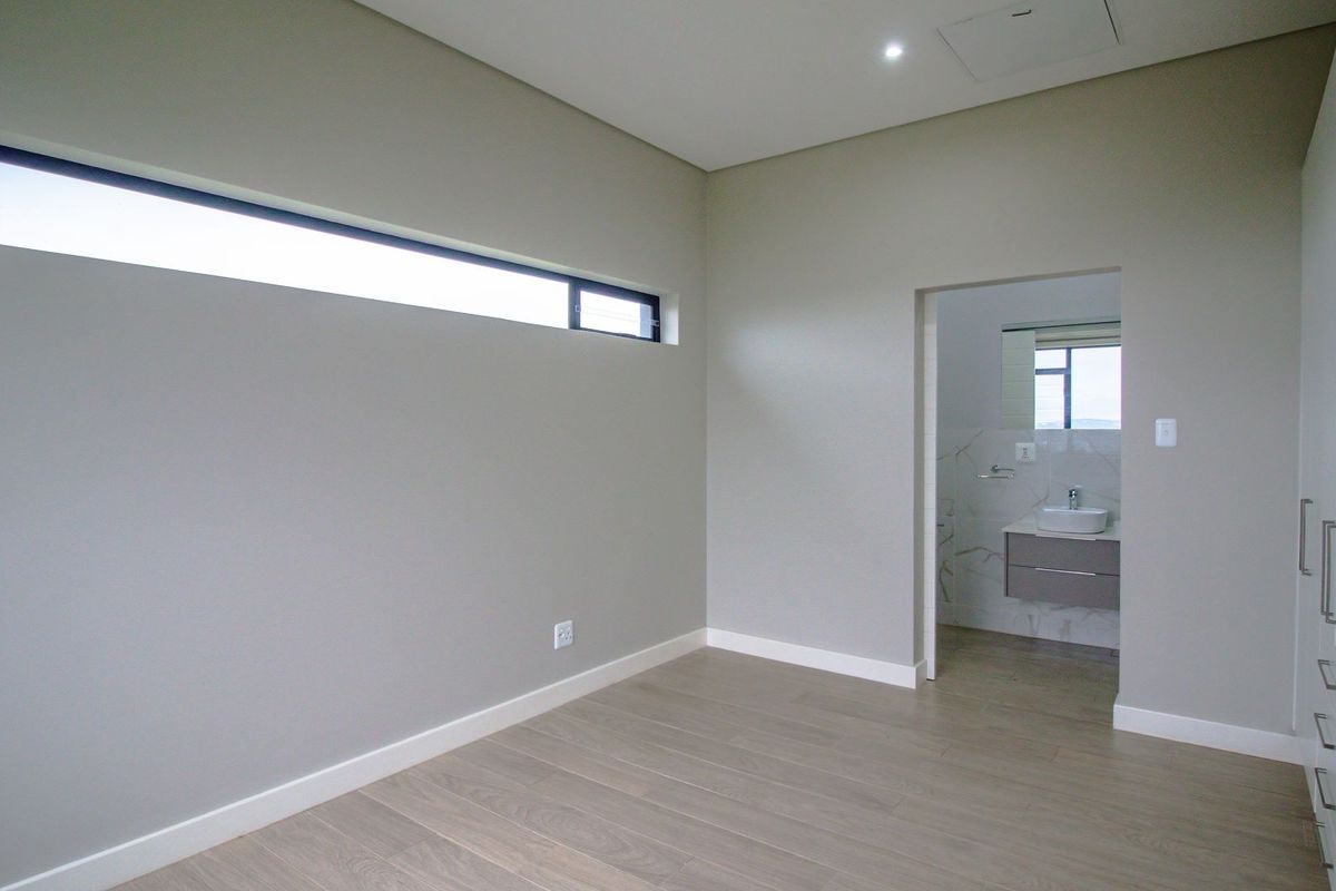 A modern, empty bedroom featuring neutral walls, laminate flooring, built-in cupboards, and an adjoining en-suite bathroom with contemporary finishes.