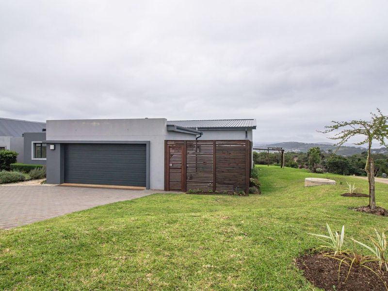 Front view of a modern house featuring a double garage, paved driveway, and timber privacy screen set within a landscaped garden.