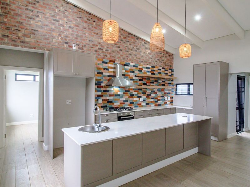 Modern kitchen featuring an exposed brick wall, vibrant mosaic backsplash, central island with quartz countertop, and high-quality built-in appliances.