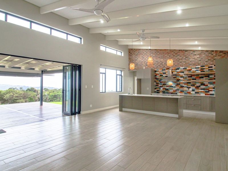 Spacious open-plan living area featuring exposed ceiling beams, a modern kitchen with a feature brick wall, and seamless access to an outdoor deck.