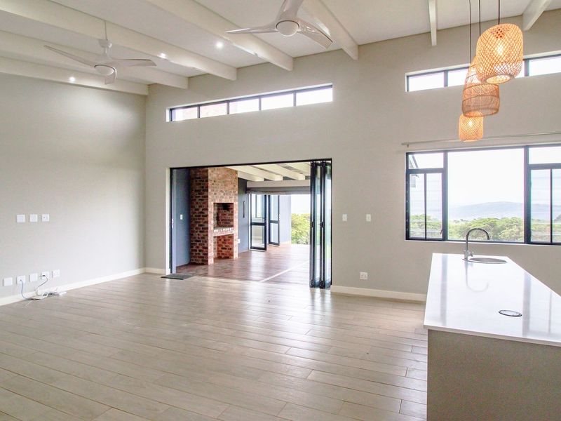 Spacious open-plan living area featuring high exposed beam ceilings, a modern kitchen island, and bi-fold doors opening to an outdoor space with a fireplace.