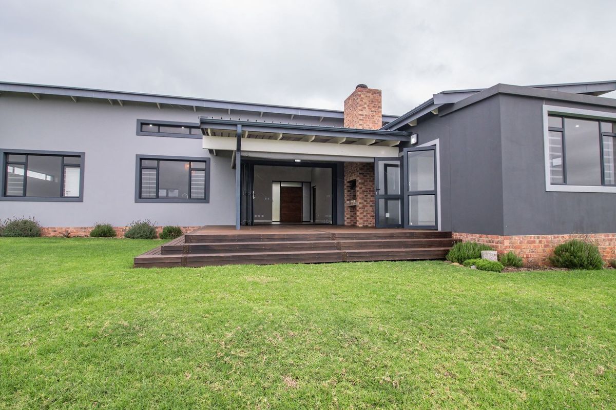 Rear view of a modern home featuring a timber deck, covered patio with a built-in brick fireplace, and expansive lawn area.