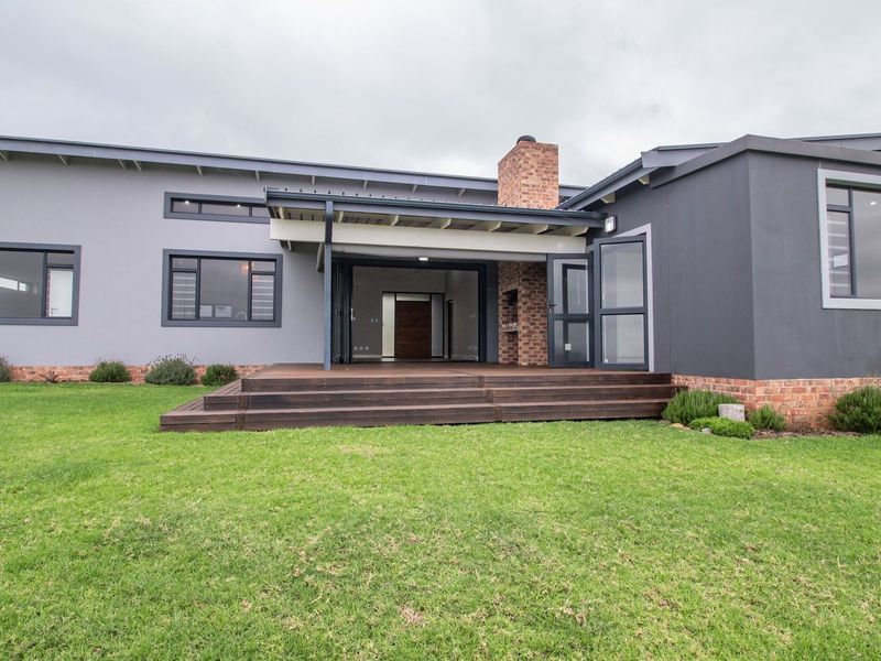 Rear view of a modern home featuring a timber deck, covered patio with a built-in brick fireplace, and expansive lawn area.