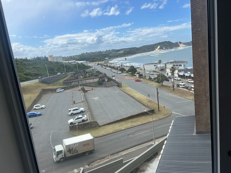 Elevated coastal view overlooking the beach, parking area, and surrounding neighbourhood from an apartment window.