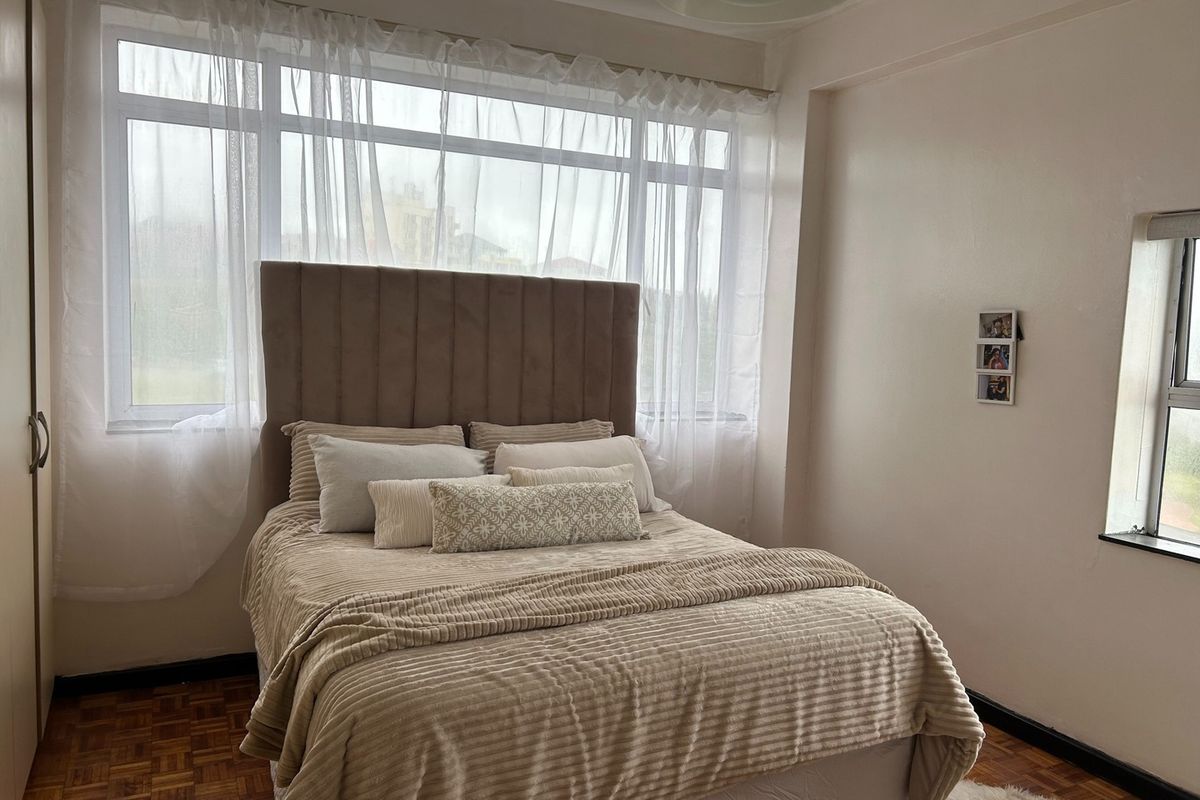 A well-lit bedroom featuring classic parquet flooring, a large window providing natural light, and a built-in wardrobe for storage.