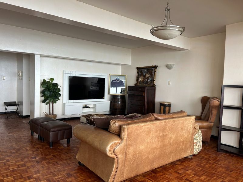 Spacious living room featuring classic parquet flooring, a wall-mounted media console, and a central pendant light fixture.