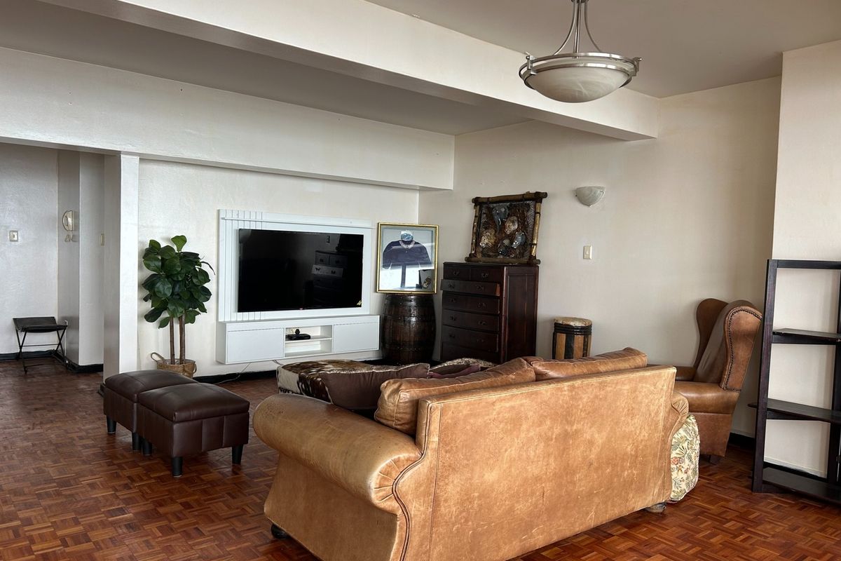 Spacious living room featuring classic parquet flooring, a wall-mounted media console, and a central pendant light fixture.
