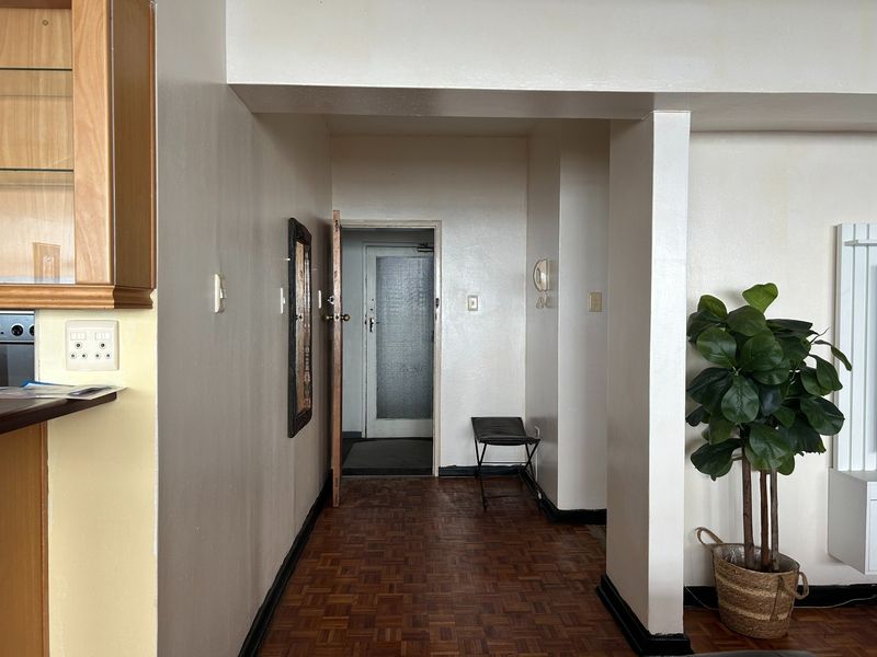 A functional apartment hallway featuring classic parquet flooring, neutral wall tones, and an integrated intercom system, providing access to the main entrance.