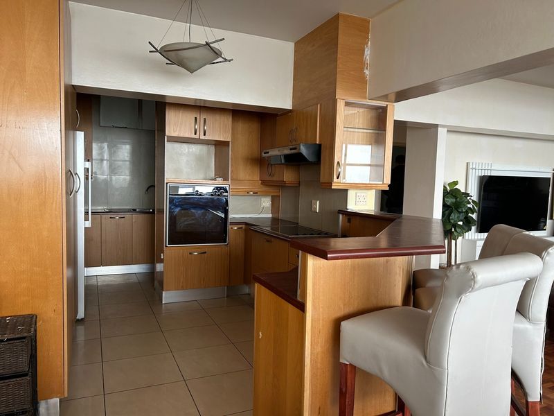 A functional kitchen featuring wood-finish cabinetry, built-in oven and hob, and a breakfast bar counter, with tiled flooring throughout.