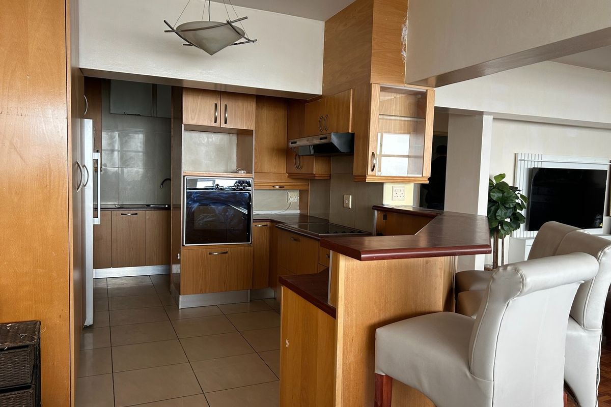 A functional kitchen featuring wood-finish cabinetry, built-in oven and hob, and a breakfast bar counter, with tiled flooring throughout.