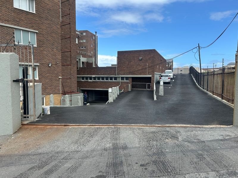 Exterior view of the apartment complex entrance featuring a brick facade, asphalt driveway, and secure underground parking access.