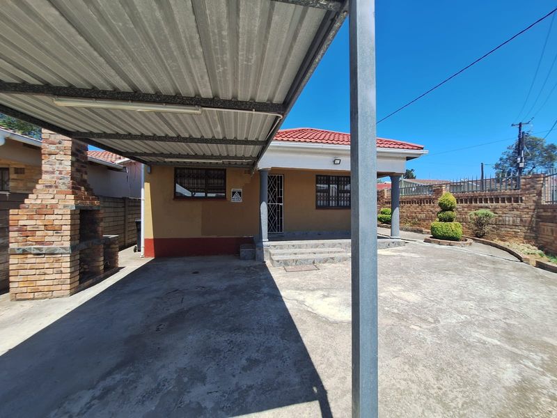 Front exterior view featuring a covered carport, built-in brick braai, and a paved driveway leading to the main entrance.