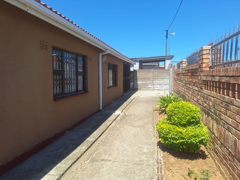 A side exterior view of the property featuring a concrete pathway, brick boundary wall with security spikes, and metal security gates.