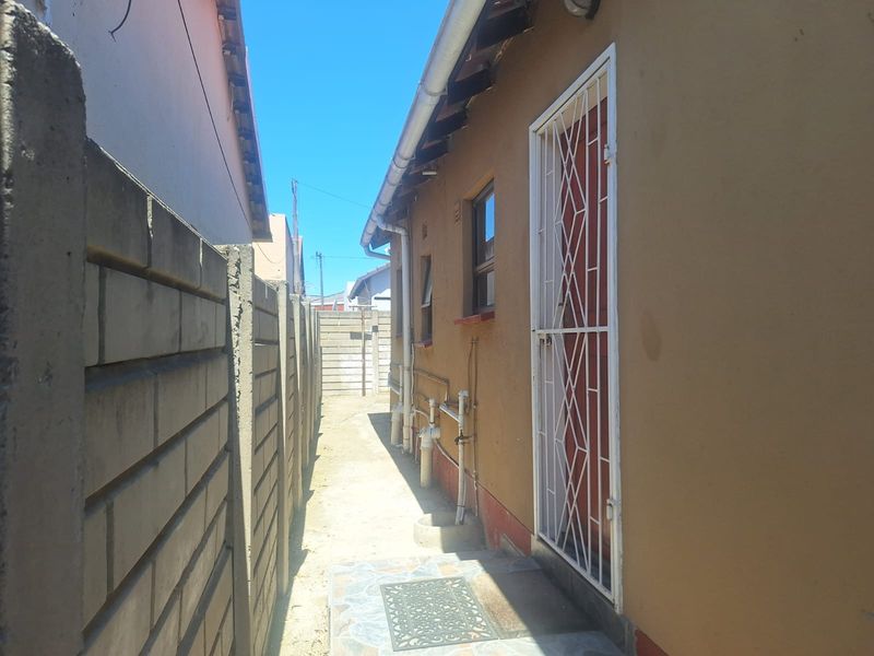 A narrow side passage of the property featuring a security gate, exposed rafters, and concrete boundary walling.