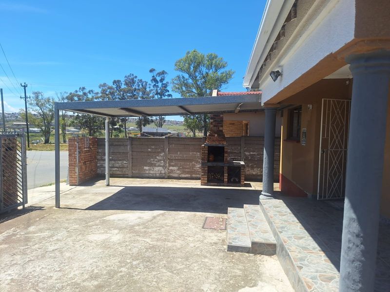 Outdoor patio area featuring a built-in brick braai, covered carport structure, and tiled entrance steps, providing a functional space for outdoor entertaining.