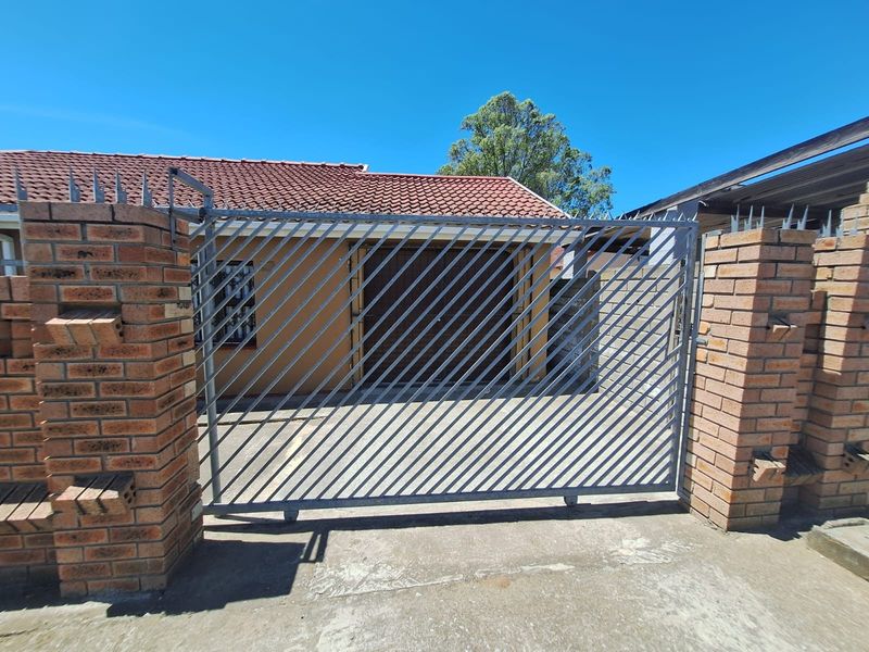 Front view of the property featuring a secure metal gate, brick perimeter wall with security spikes, and a tiled roof structure.