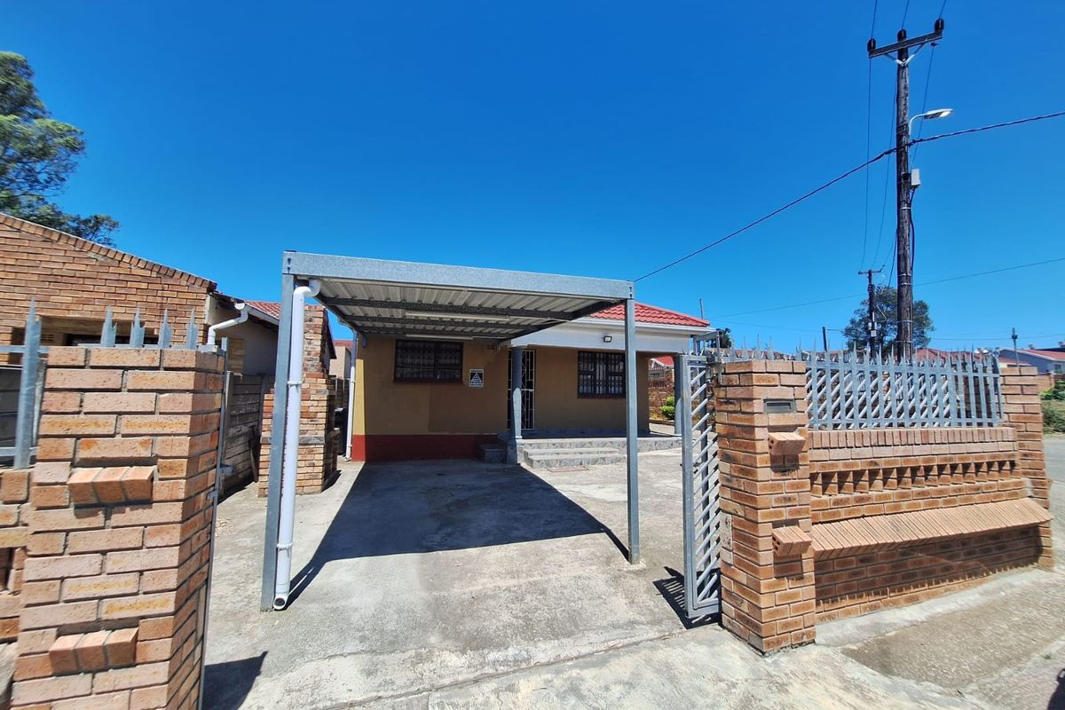 Front view of the property featuring a metal carport, brick boundary wall with security gate, and tiled roof.
