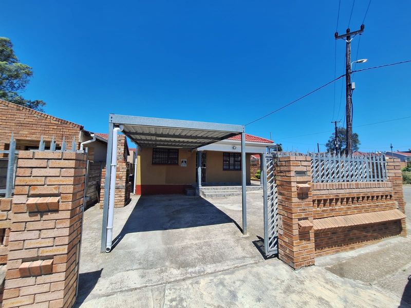 Front view of the property featuring a metal carport, brick boundary wall with security gate, and tiled roof.
